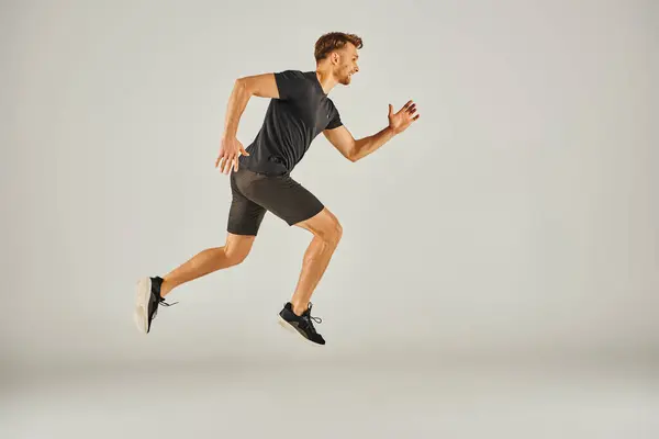 stock image A young athletic man in active wear is energetically running on a grey background in a studio setting.