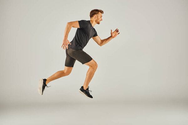 A young athletic man in active wear is energetically running on a grey background in a studio setting.