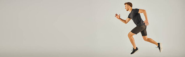 Молодой спортсмен в активной одежде энергично бегает на сером фоне в студии.