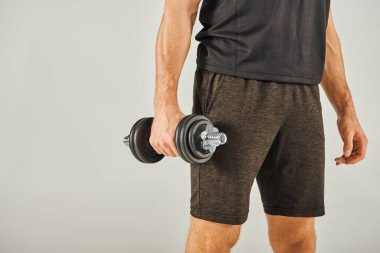 Aktif giyinen genç bir sporcu, gri arka planı olan bir stüdyoda bir çift dambılı kaldırır..
