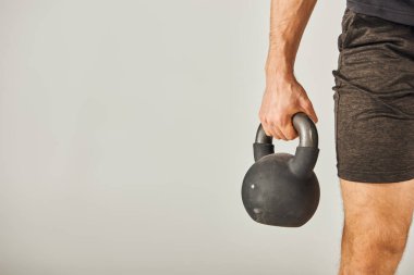 Aktif giyinen genç bir sporcu, gri arka planı olan bir stüdyoda kettlebell kaldırıyor..