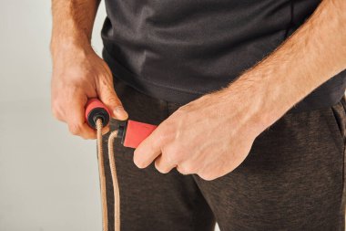 Aktif giyinen genç bir sporcu, atlama halatını gri bir arka plana karşı bir stüdyoda kararlılıkla çekiyor..