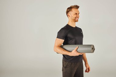 Aktif giyinen genç bir sporcu, beyaz arka planlı bir stüdyoda yoga minderi tutuyor..
