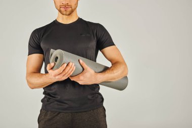 Aktif çalışan genç sporcu gri bir geçmişi olan bir stüdyoda yoga minderi tutuyor..