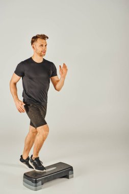 Aktif çalışan genç bir sporcu, atölyede beyaz bir arka plana karşı bir basamakla enerjik bir şekilde koşuyor..