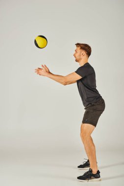 A young sportsman in active wear catches a yellow and black ball in a dynamic studio setting with a grey background. clipart