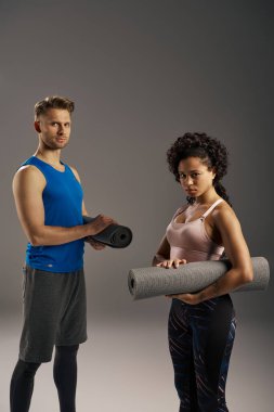 Young multicultural couple in active wear standing gracefully next to a yoga mat in a studio setting. clipart