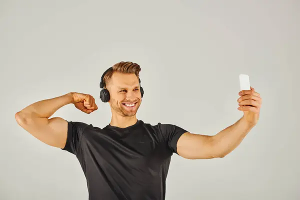 stock image A young sportsman in active wear taking a selfie with his phone in a studio with a grey background.