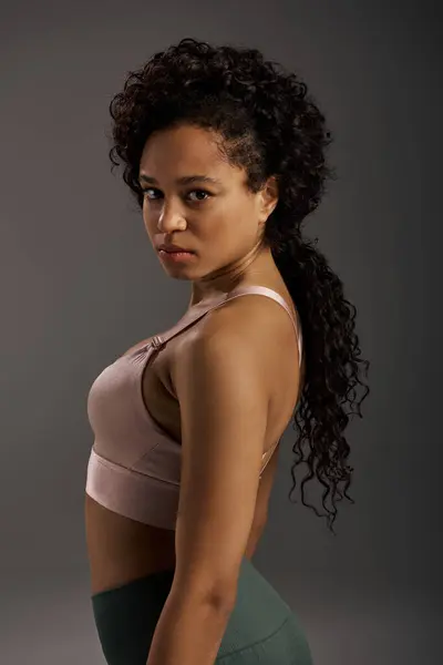 stock image Curly African American sportswoman in active wear working out in a studio with a grey background.