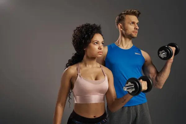 stock image Multicultural man and woman in active wear pose confidently with dumbbells in a studio setting.