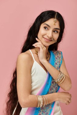 Young indian woman in blue and white sari poses gracefully on pink background. clipart