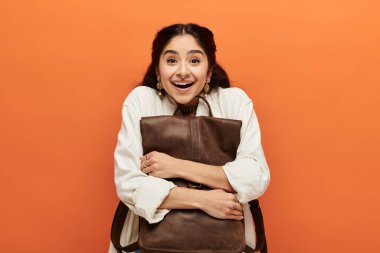 Young indian woman happily holding a brown backpack. clipart