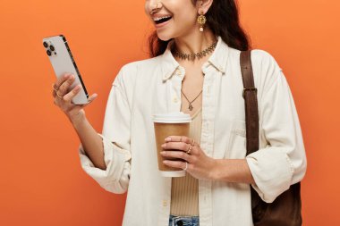Genç Hintli kadın elinde kahve ve telefonla birden fazla iş yapıyor..