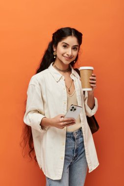 Tarz sahibi genç bir Hintli kadın elinde turuncu bir arka planda bir fincan kahve tutuyor..