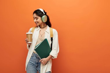 Genç Hintli kadın elinde kahve fincanı tutarken kulaklıkla müzik dinliyor..