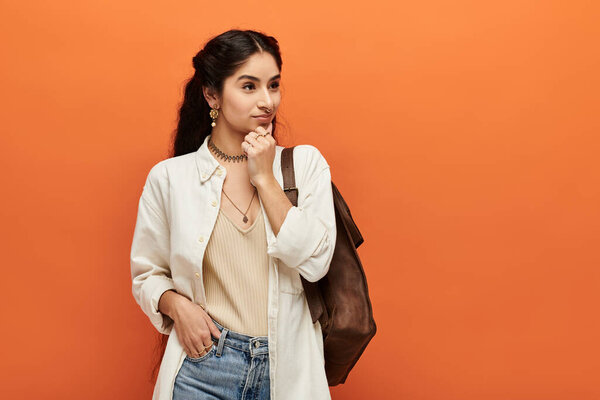 Стильная молодая индианка в джинсах и белой рубашке уверенно позирует против яркой оранжевой стены.