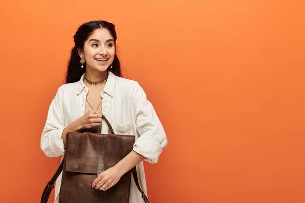 индийская женщина держит коричневый рюкзак на ярко-оранжевом фоне.