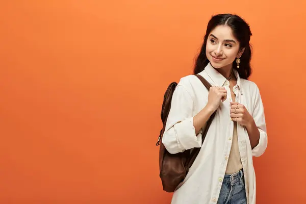 Young Indian Woman Confidently Stands Backpack Vibrant Orange Backdrop — Stok fotoğraf