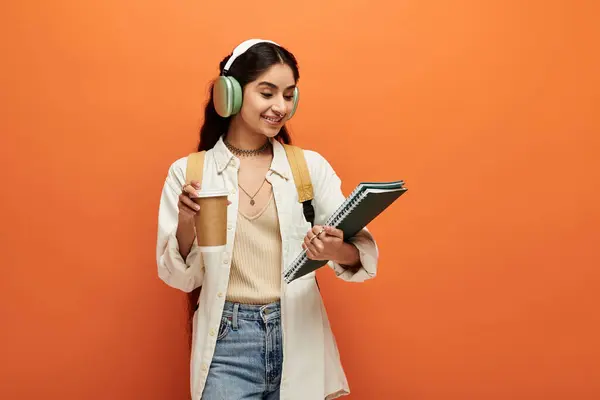 stock image Young indian woman with headphones, notebook, and coffee, deep in thought.