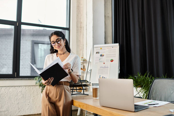 businessindian woman standing by a window, holding a notebook.