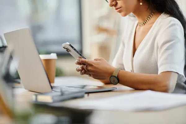 stock image A young indian woman using phone at desk.