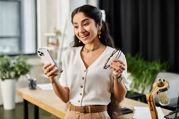 stock image A young indian woman energetically holds a smartphone in her hand.