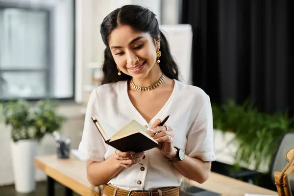 stock image Young indian woman engages in writing in office space.