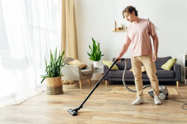Ev elbiseli yakışıklı bir adam oturma odasını temizlemek için süpürge kullanıyor..