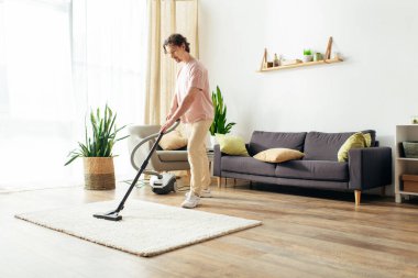 Ev kıyafetleri içinde yakışıklı bir adam evini elektrikli süpürge ile temizliyor..