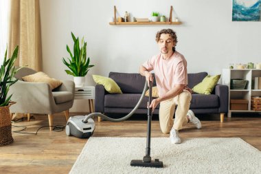 A handsome man in cozy homewear diligently vacuuming a living room. clipart