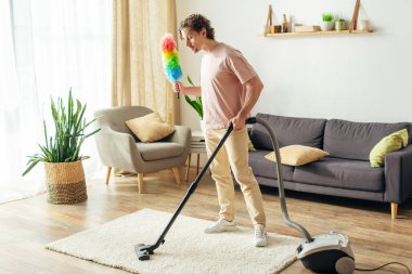 Ev elbiseli bir adam oturma odasını süpürgeyle temizliyor..