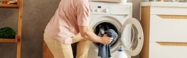 Elbiseleri çamaşır makinesine dikkatlice yerleştiren bir adam..