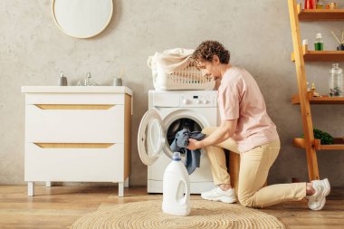 Çamaşır makinesinin önünde çamaşır yıkayan adam..