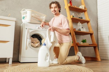 A handsome man in a pink shirt meticulously doing laundry at home. clipart