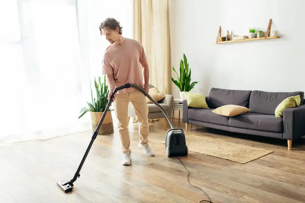 stock image A man in cozy homewear cleans the living room with a vacuum.
