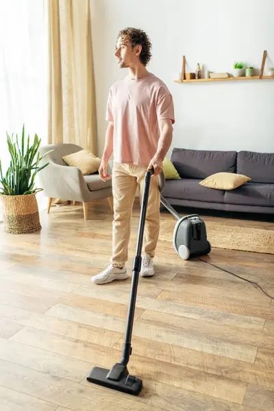 stock image Handsome man in cozy homewear vacuuming on hardwood floor.