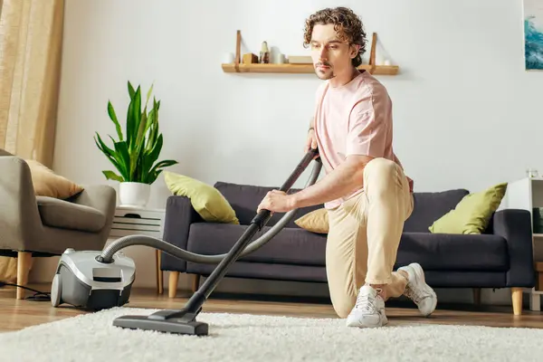 stock image A man in cozy homewear vacuums the living room.