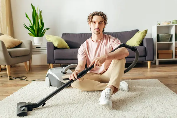 stock image A handsome man in cozy homewear sits on the floor with a vacuum.