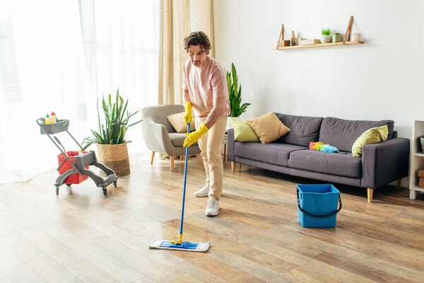 Handsome man in cozy homewear cleaning his living room with a mop.