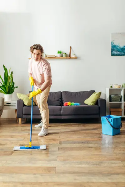 stock image Handsome man in cozy homewear cleaning floor with mop.