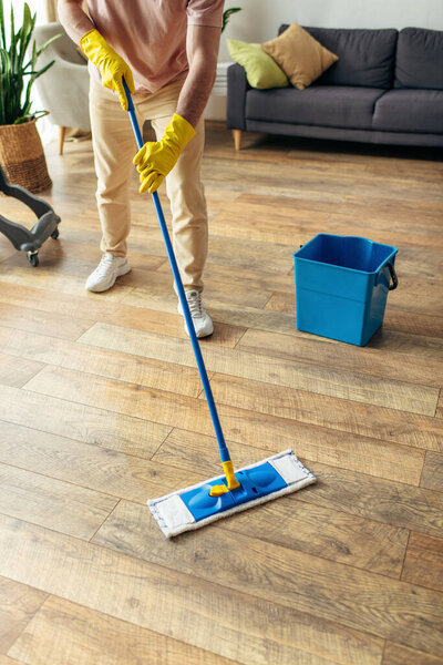 A handsome man in cozy homewear diligently mopping the floor.