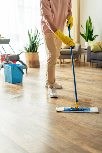 A handsome man in cozy homewear mops the floor.