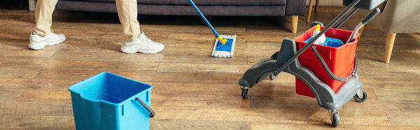 A handsome man in cozy homewear uses a mop to clean the floor.