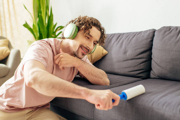Handsome man in cozy home attire sitting near a couch, lost in music with headphones.