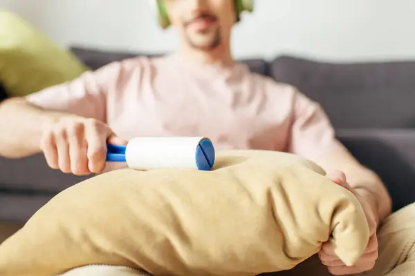 stock image A man in cozy homewear sitting on a couch, holding a sticky roller.