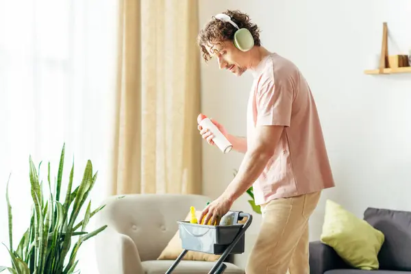 stock image A handsome man in cozy homewear cleans a living room while wearing headphones.