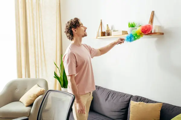 stock image A handsome man in cozy homewear cleaning a living room with a duster.