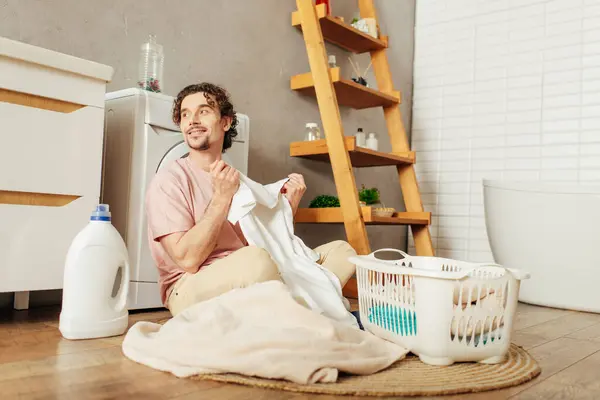 Stock image Handsome man in homewear sitting on floor sorting laundry.