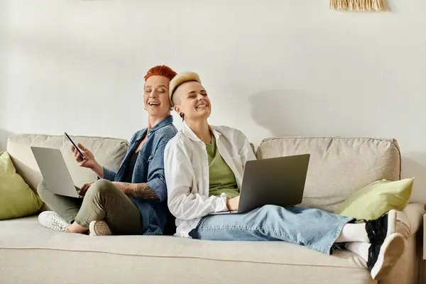 Stock image Two women with laptops sit on a couch, engrossed in work, creating connection.