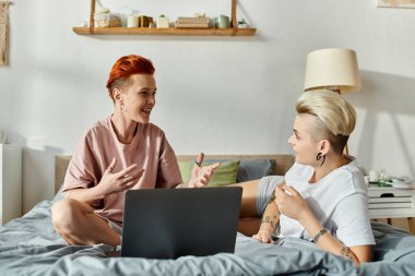 Kısa saçlı lezbiyen bir çift bir yatakta oturmuş, dizüstü bilgisayar kullanırken derin sohbetler ediyorlar..